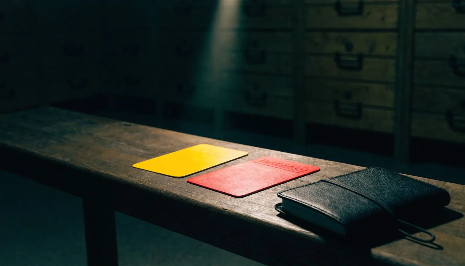Tarjetas amarilla y roja junto a un cuaderno de árbitro en un banco de vestuario